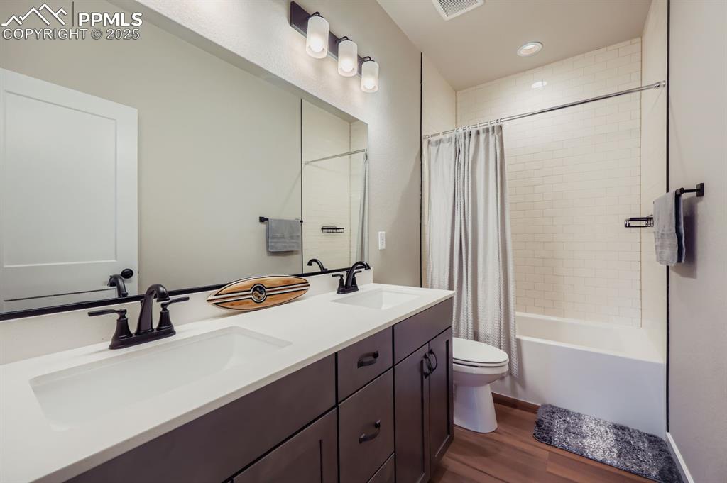 Image 18 of 28: Full bath with double vanity, dark wood finished floors, shower / tub combo