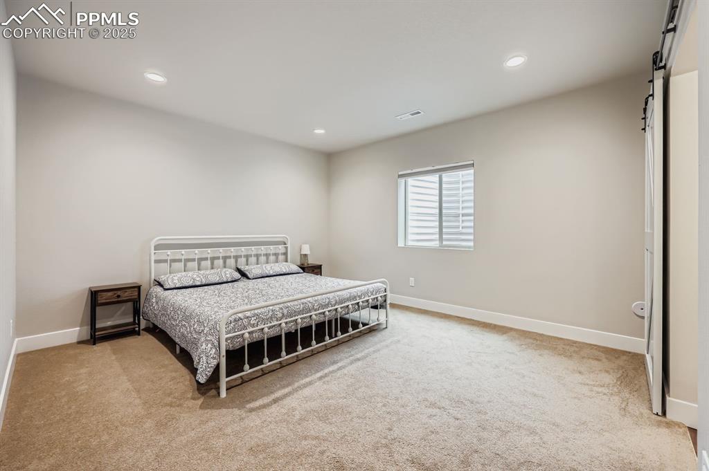 Image 22 of 28: Bedroom with a barn door, light carpet, and recessed lighting