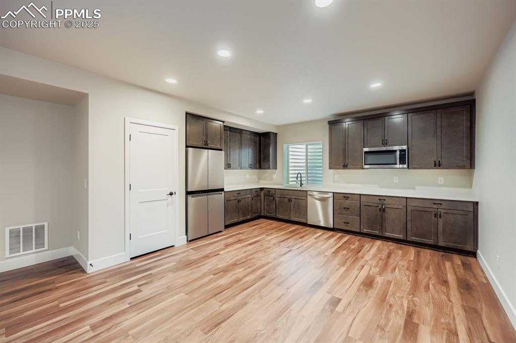 Image 25 of 28: Kitchen with dark brown cabinetry, light countertops, stainless steel appli