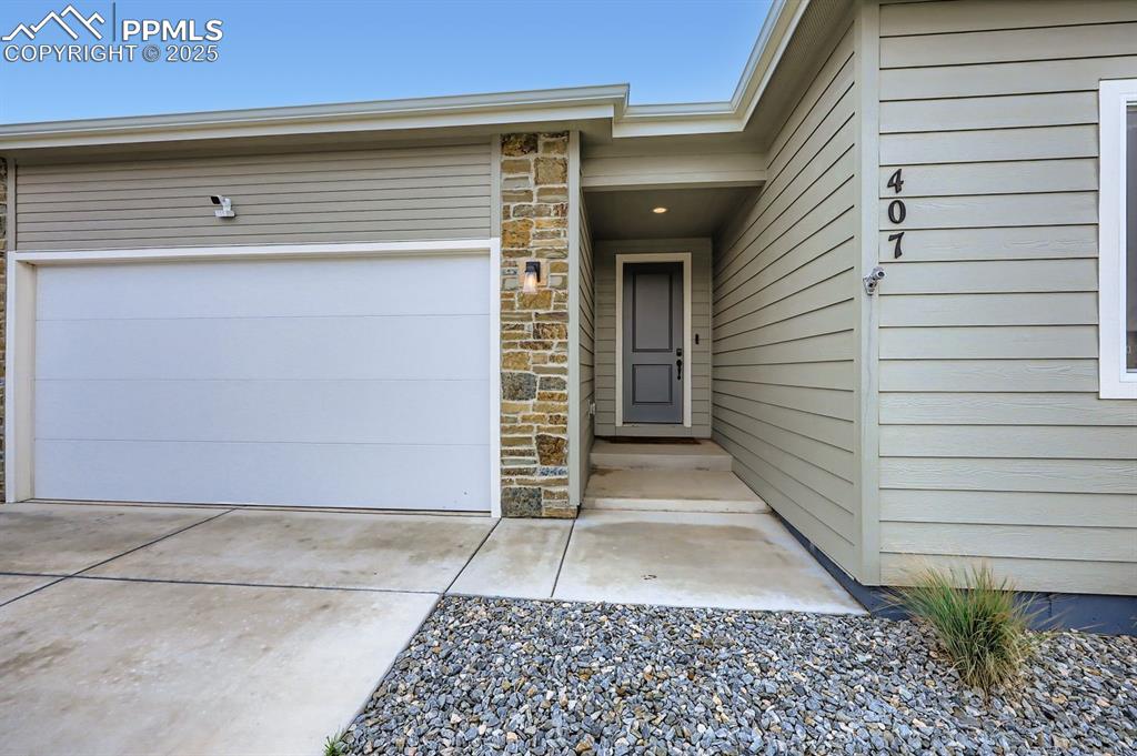 Image 3 of 28: Doorway to property with stone siding, a garage, and driveway
