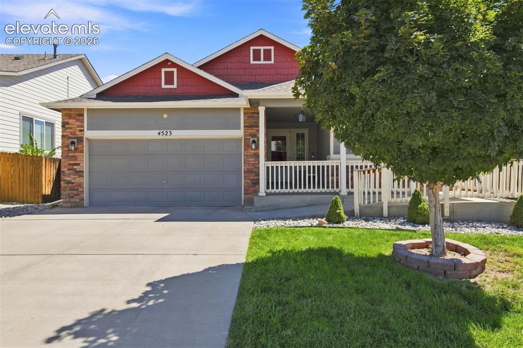 Caption: Covered front porch with white railing, brick facade accents, attached two-car garage, concrete driv