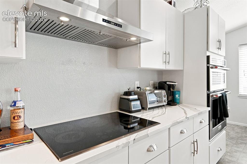 Image 11 of 32: Sleek stainless steel range hood, built-in cooktop, light-toned cabinetry, 