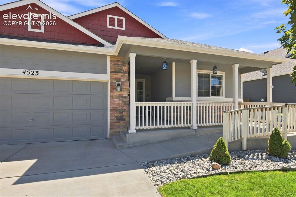 Image 4 of 32: Covered front porch with white railings, stone façade accents, and a wide c