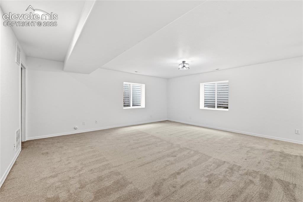 Image 19 of 30: Spacious room featuring neutral carpeting, two windows with horizontal blin