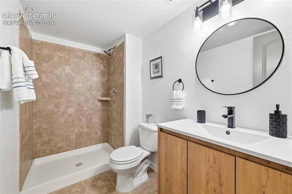 Image 22 of 30: Bathroom featuring a tiled standing shower, white toilet, and a wood-finish