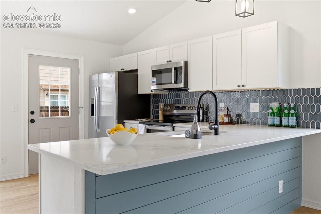 Image 6 of 30: Kitchen featuring a spacious island with a white countertop and blue shipla