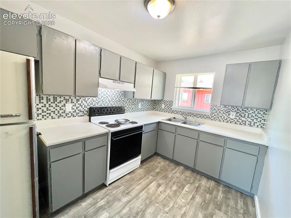 Image 11 of 23: Kitchen featuring wood-finish flooring, grey cabinetry, mosaic tile backspl