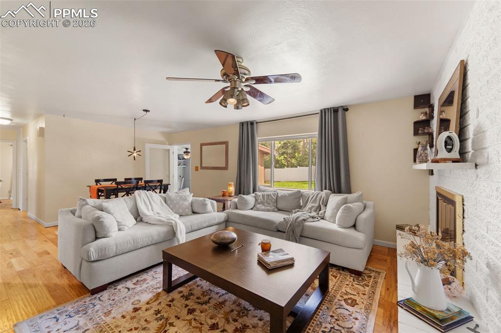 Image 15 of 41: Living room featuring wood finished floors, a ceiling fan, and a fireplace