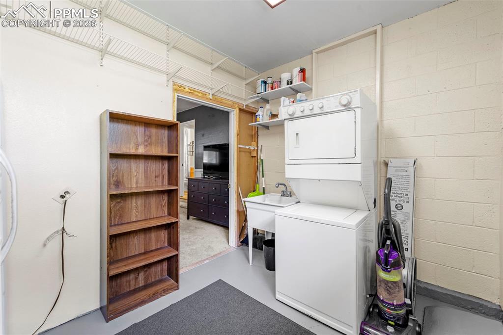 Image 26 of 41: Laundry room featuring stacked washing machine and dryer, concrete floors,
