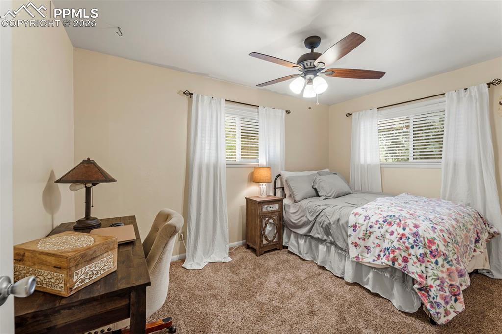Image 27 of 41: Bedroom with carpet floors, a ceiling fan, multiple windows, and an office