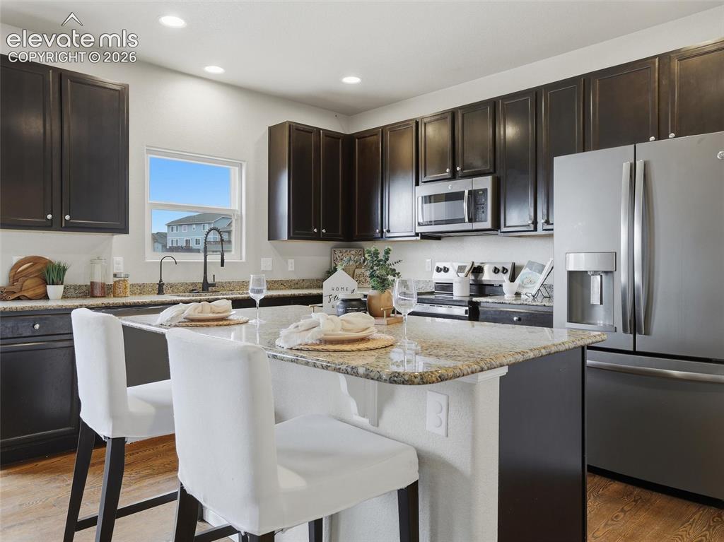 Image 11 of 45: Kitchen featuring dark wood cabinetry, granite countertops, stainless steel