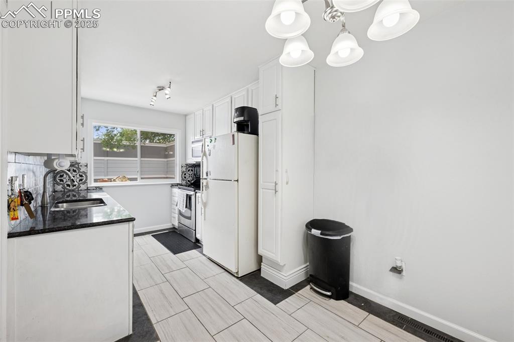 Image 7 of 31: Kitchen featuring white appliances, white cabinetry, backsplash, a chandeli