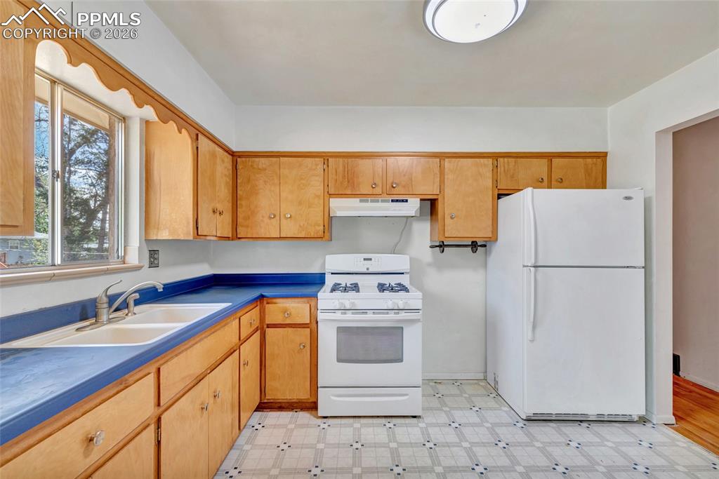 Image 10 of 36: Kitchen featuring wood cabinetry, blue countertops, white appliances, and p
