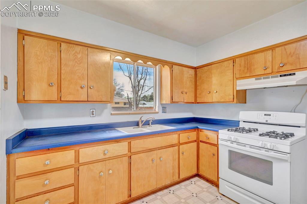 Image 11 of 36: Kitchen with wood cabinetry, blue countertops, and white appliances