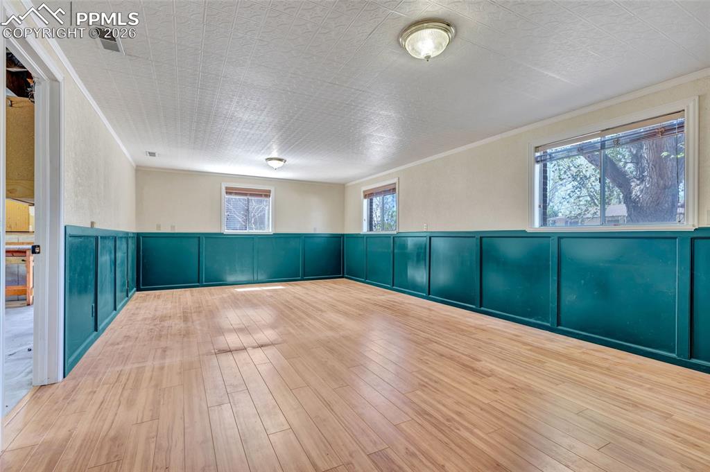 Image 22 of 36: Spacious room featuring wood-finish flooring, half-wall teal wainscoting, a