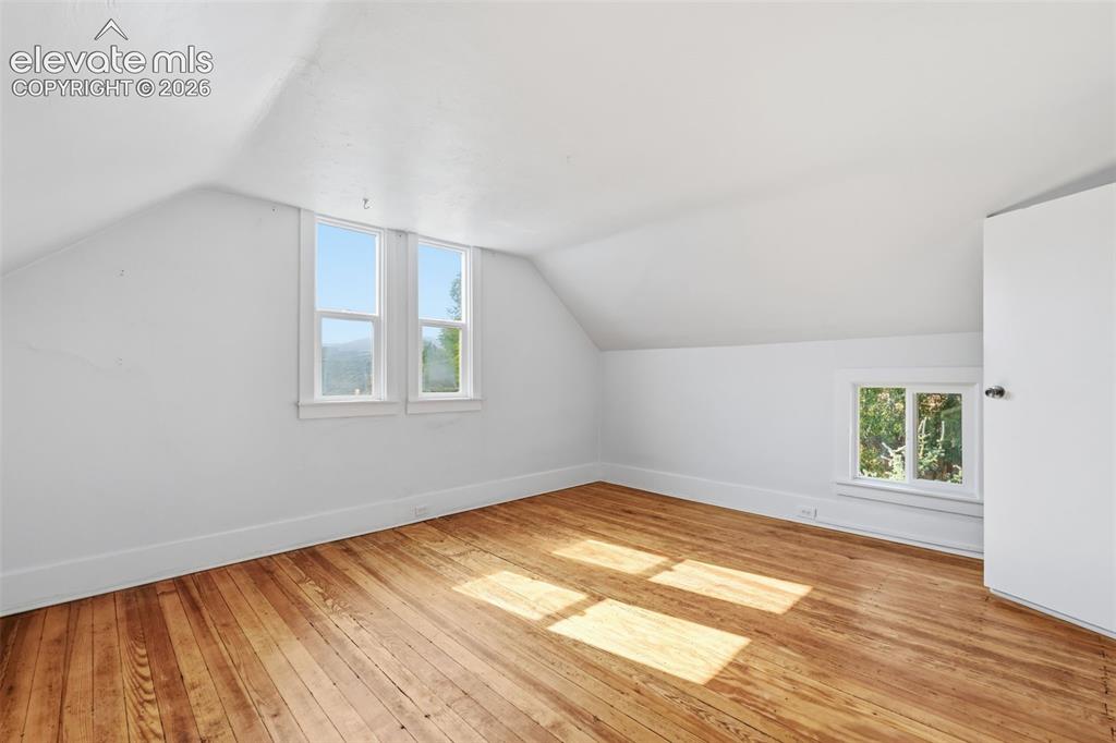 Image 24 of 40: Primary bedroom with sloped ceilings, pine hardwood flooring, two large win