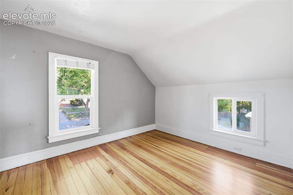 Image 28 of 40: Secondary upper bedroom with pine hardwood flooring, sloped ceiling, and a