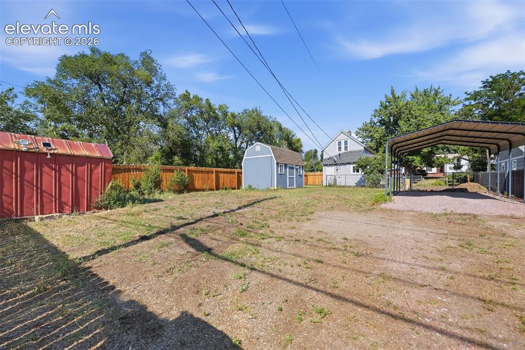 Image 34 of 40: Expansive property featuring a red storage shed, blue storage shed, wood pr