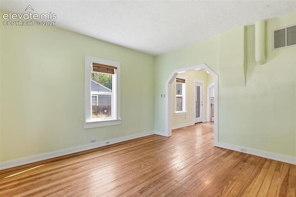 Image 8 of 40: Living room with pine hardwood flooring throughout, arched opening, and whi