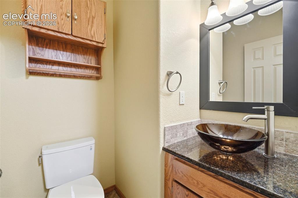 Image 15 of 40: Bathroom vanity featuring a vessel sink, dark countertop, and wood-finish c