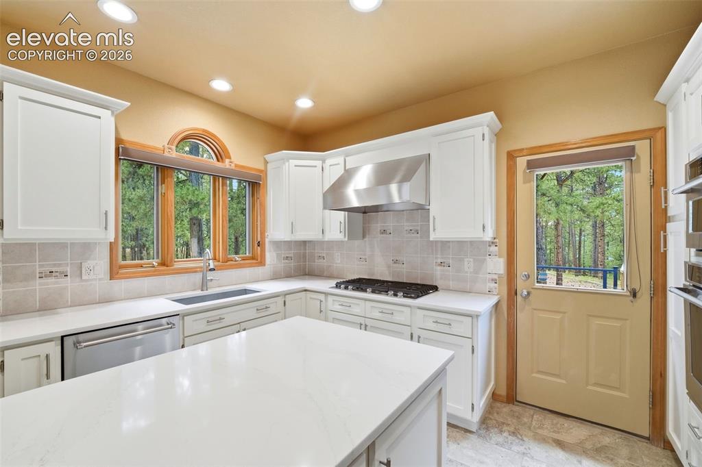 Image 6 of 40: Kitchen featuring white cabinetry, light-toned countertops, tile backsplash