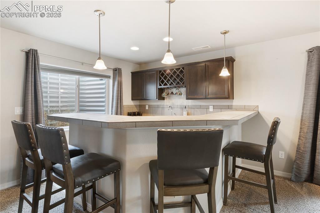 Image 26 of 41: Downstairs mini bar area with seating, pendant lighting, and great space fo
