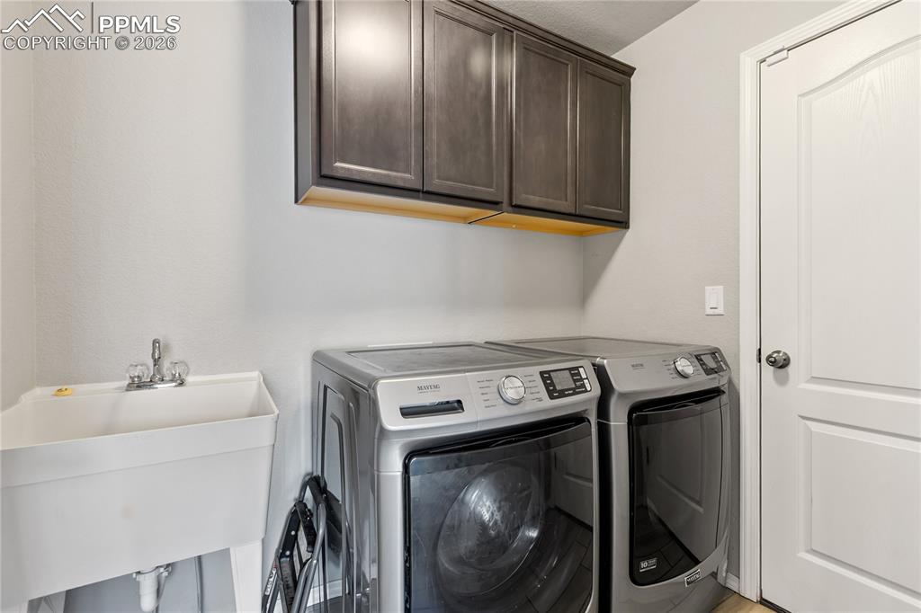 Image 33 of 41: Convenient laundry room with upper cabinetry and utility sink