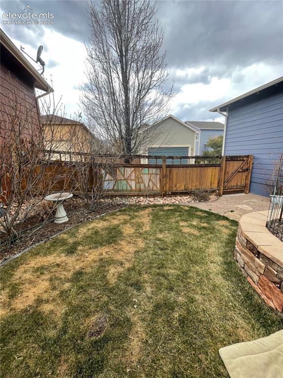 Image 25 of 27: Enclosed yard featuring a wood fence, stone retaining wall, and gravel path