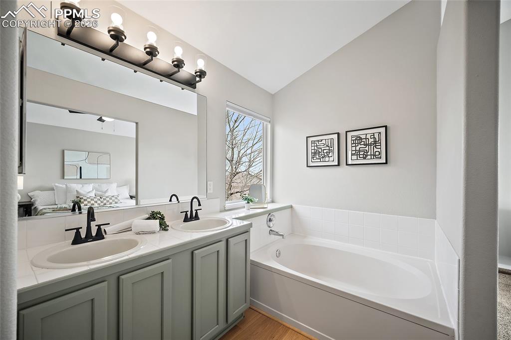 Image 18 of 46: Full bathroom with double vanity, vaulted ceiling, a bath, light wood-style