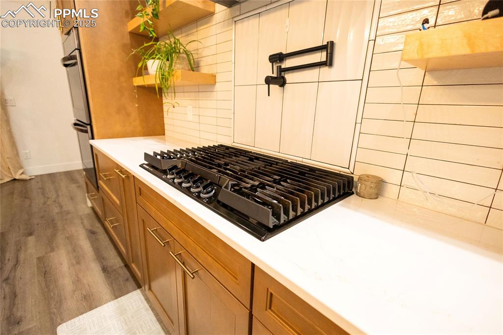 Image 40 of 44: Kitchen featuring black gas stovetop, brown cabinetry, light wood-style flo