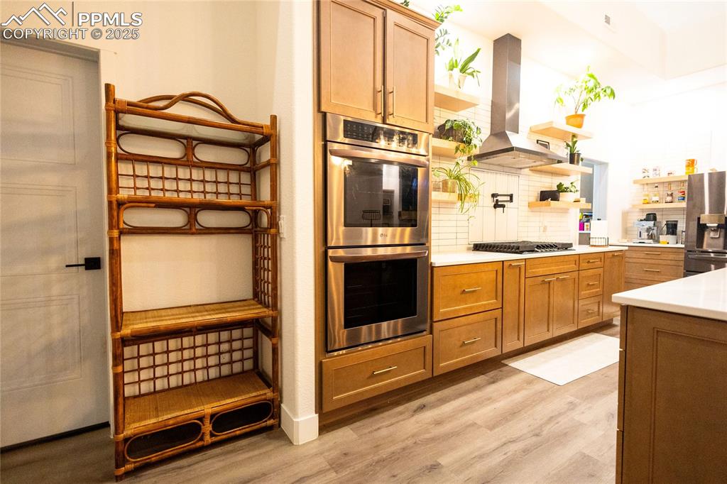 Image 41 of 44: Kitchen with brown cabinetry, open shelves, appliances with stainless steel