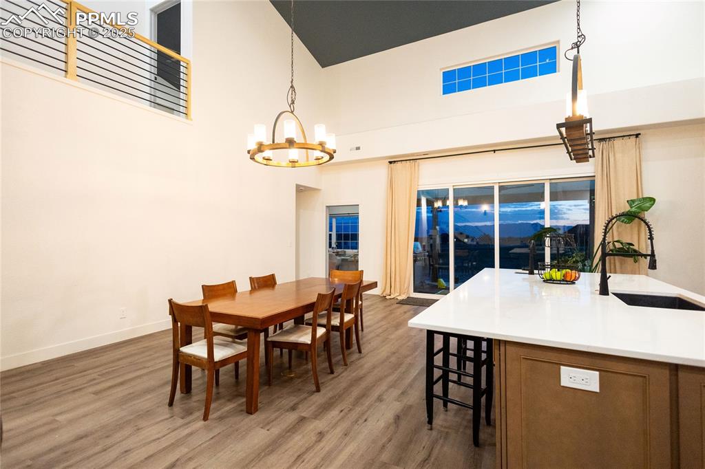Image 42 of 44: Dining area featuring wood finished floors, a towering ceiling, and a chand