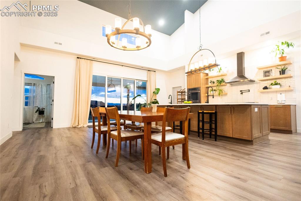 Image 6 of 44: Dining area featuring a high ceiling, light wood-type flooring, and a chand