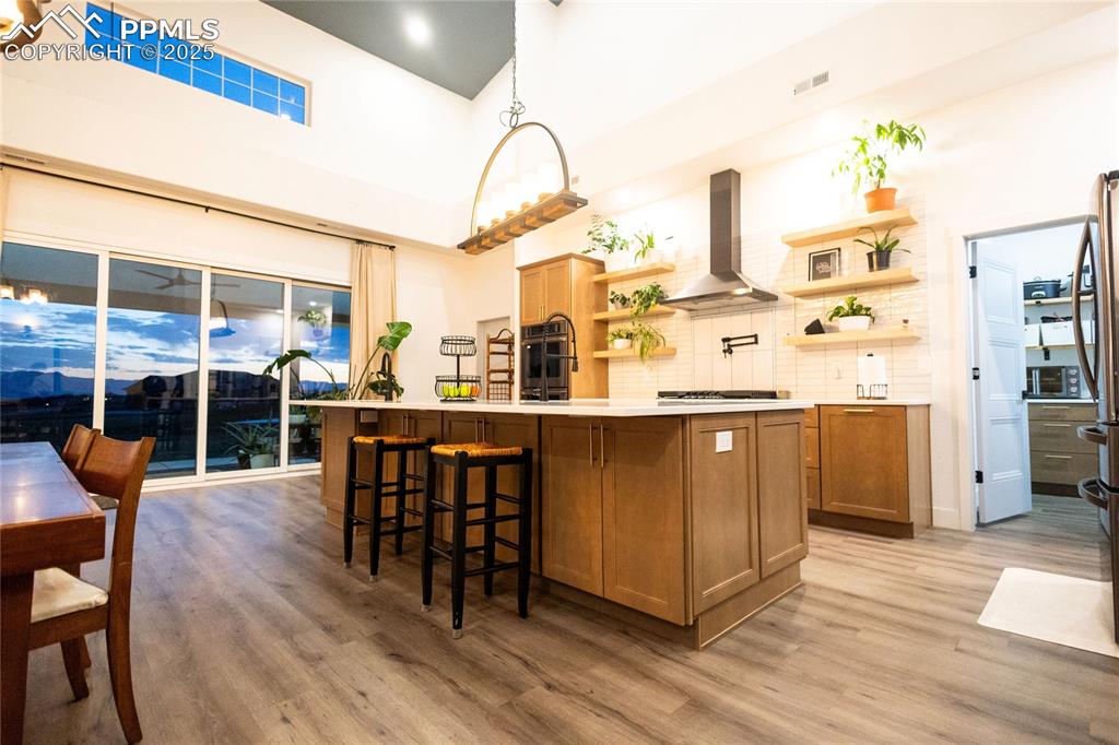 Image 7 of 44: Kitchen featuring open shelves, backsplash, brown cabinets, a high ceiling,