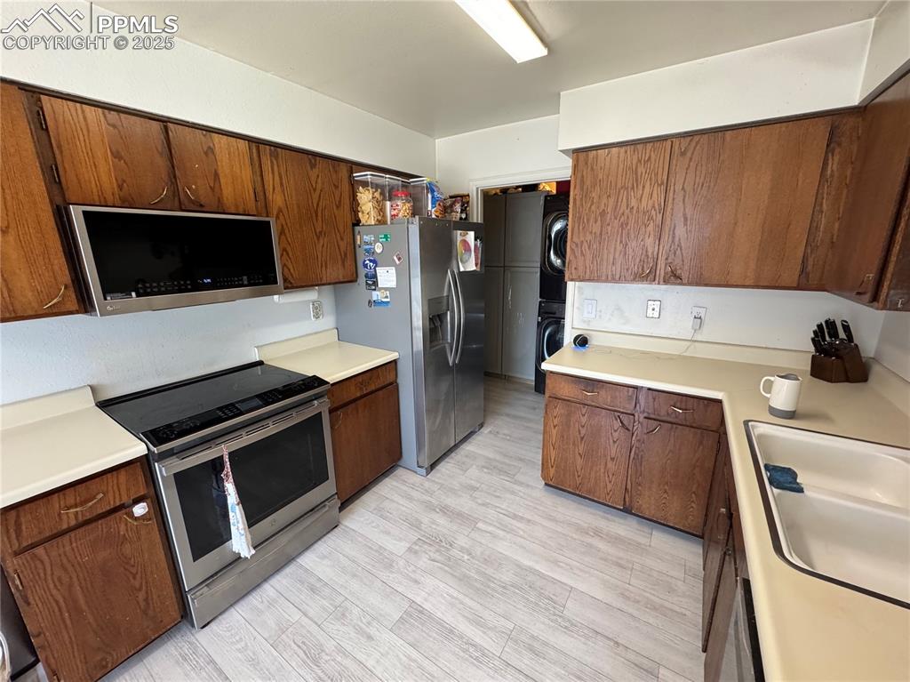 Image 13 of 22: Kitchen with stainless steel appliances, stacked washer / dryer, light wood