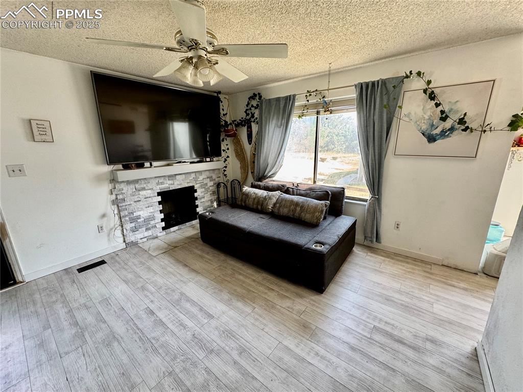 Image 3 of 22: Living area with a stone fireplace, a textured ceiling, wood finished floor