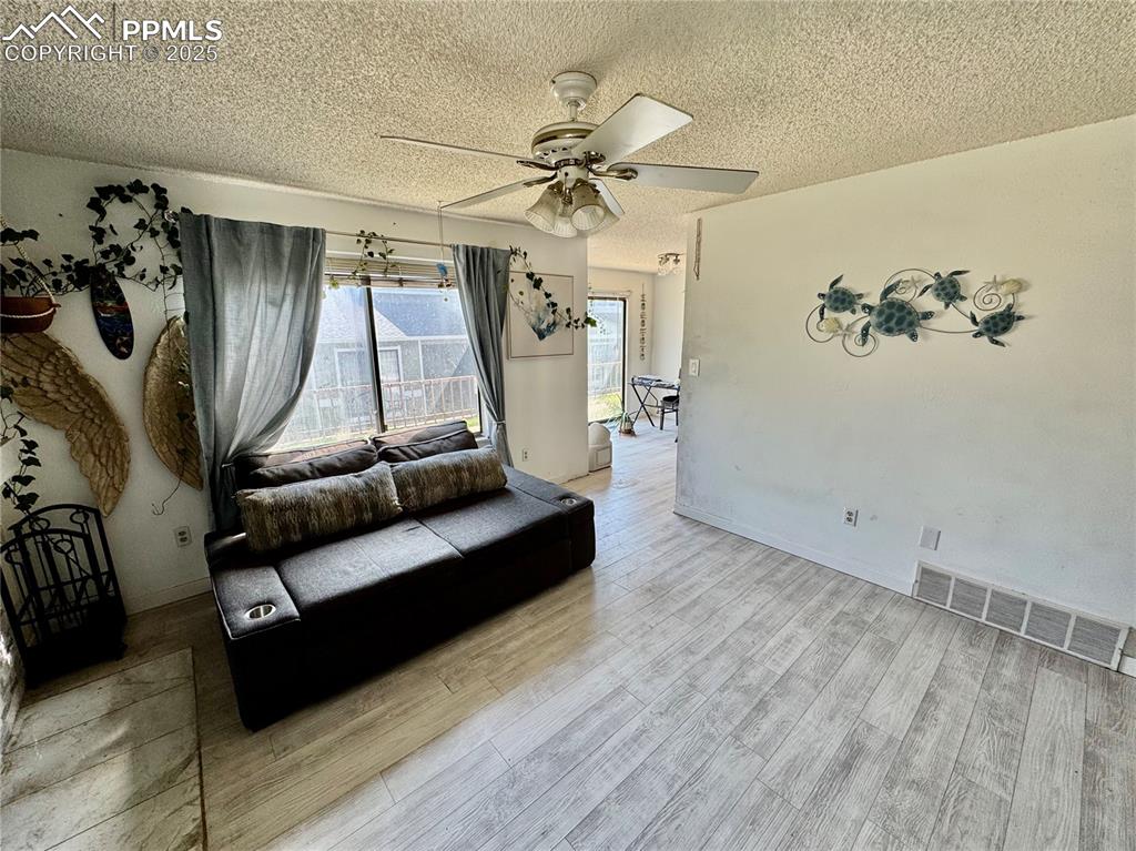 Image 4 of 22: Living area with a textured ceiling, wood finished floors, and a ceiling fa