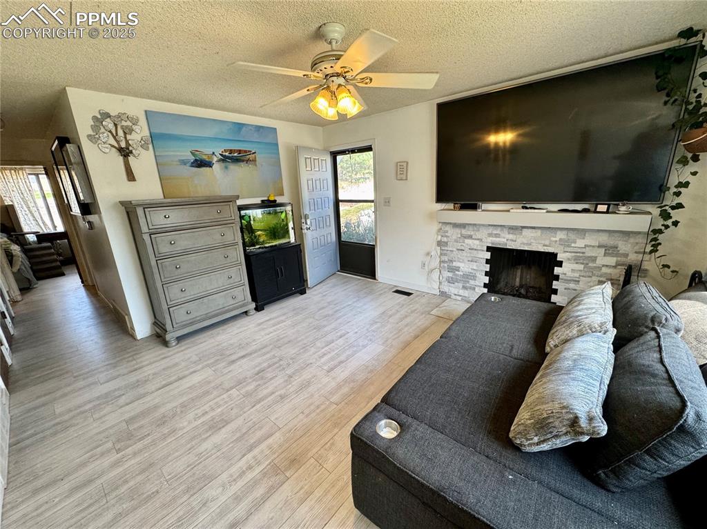 Image 5 of 22: Living room with a textured ceiling, a brick fireplace, light wood finished