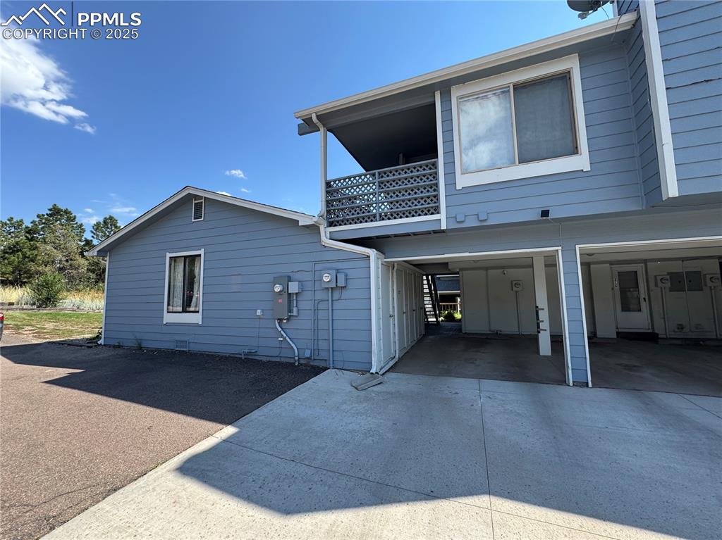 Image 8 of 22: View of side of property featuring a carport, driveway, a balcony, and a pa