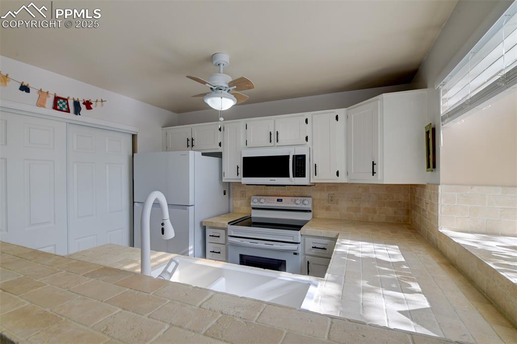 Image 7 of 25: Kitchen with white appliances, white cabinets, tile countertops, a ceiling 