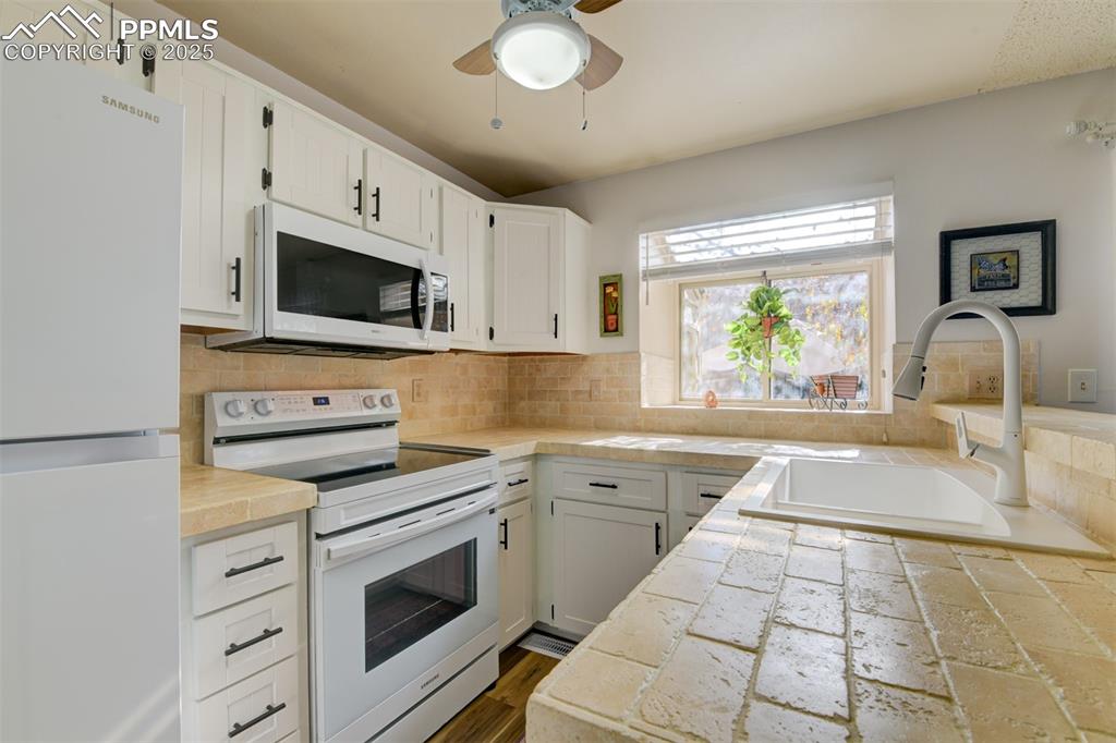 Image 8 of 25: Kitchen with white appliances, decorative backsplash, white cabinetry, and 