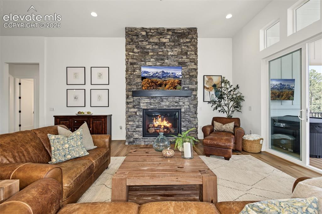 Image 10 of 50: Stone-clad fireplace with a dark mantel, wood-finish flooring, white walls,