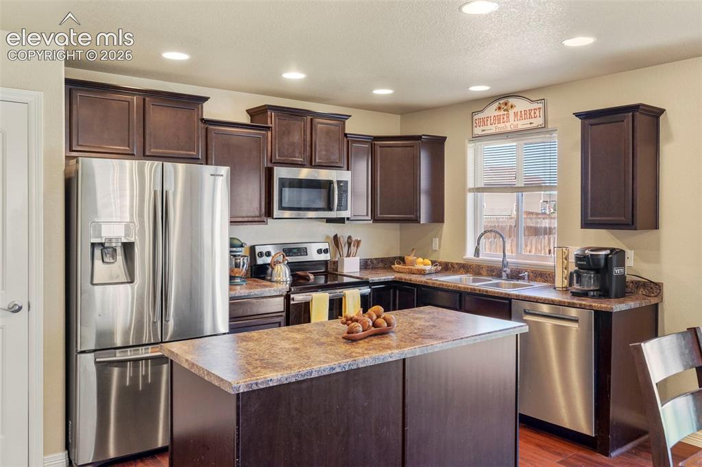 Image 10 of 32: Kitchen featuring dark wood cabinetry, stainless steel appliances, a center