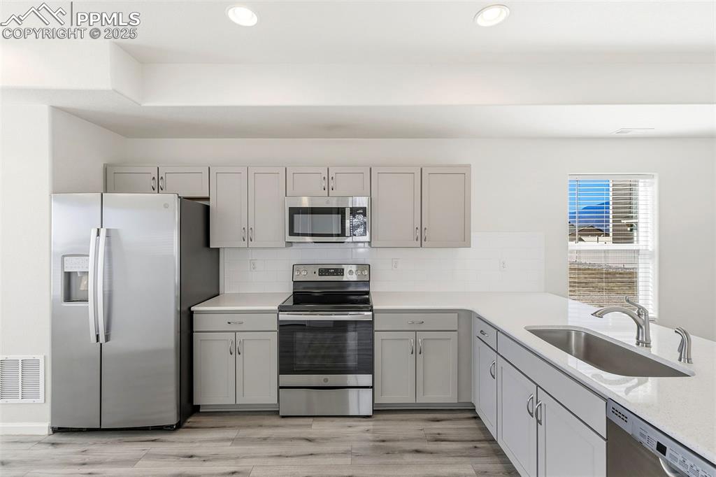Image 13 of 35: Kitchen featuring appliances with stainless steel finishes, gray cabinetry,