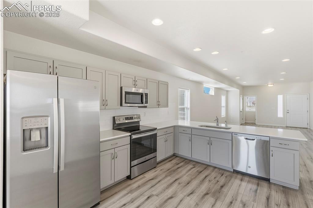 Image 14 of 35: Kitchen with appliances with stainless steel finishes, gray cabinetry, ligh