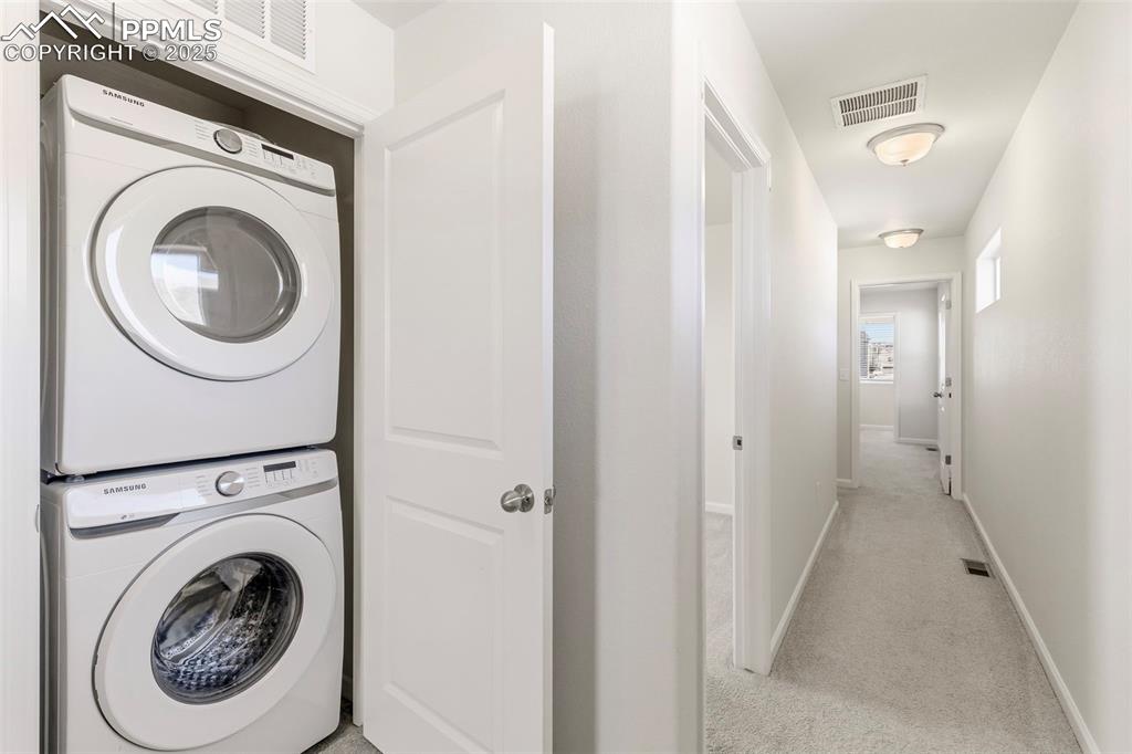 Image 26 of 35: Laundry room featuring light carpet and estacked washer and dryer