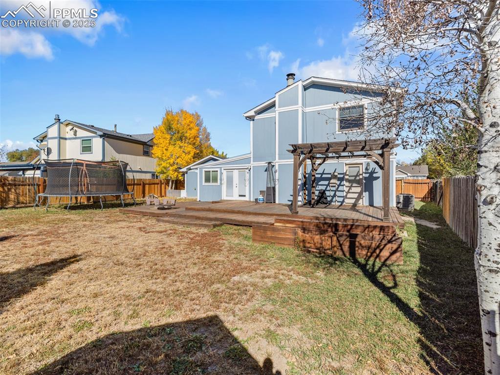 Image 26 of 29: Back of property with a fenced backyard, a deck, a trampoline, and a chimne