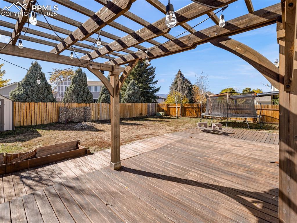 Image 29 of 29: Deck featuring a trampoline, a fenced backyard, and a pergola