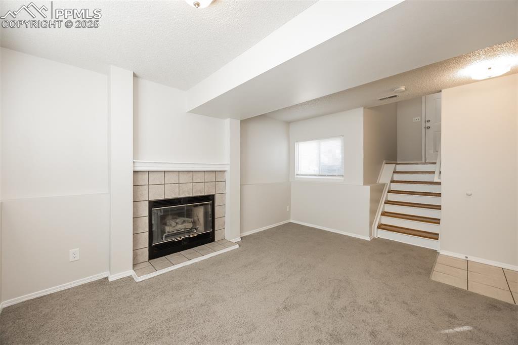 Image 11 of 25: Unfurnished living room with carpet flooring, a textured ceiling, a firepla