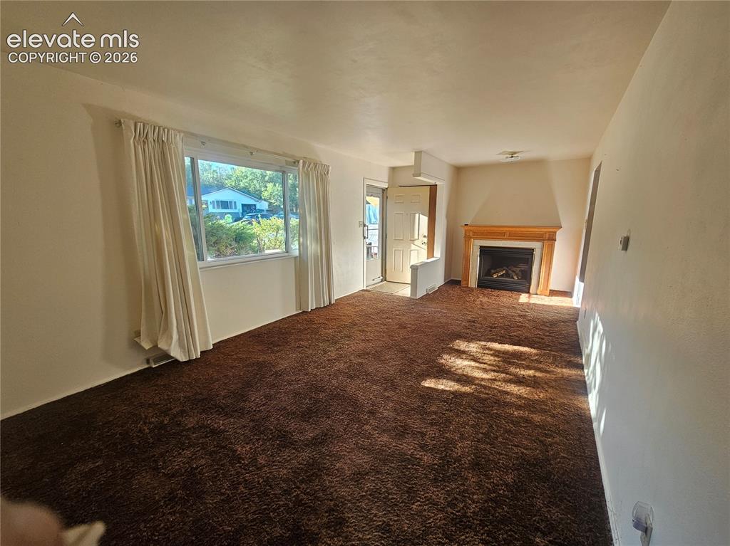 Image 10 of 37: Spacious room, large window, and a fireplace with a wood mantel